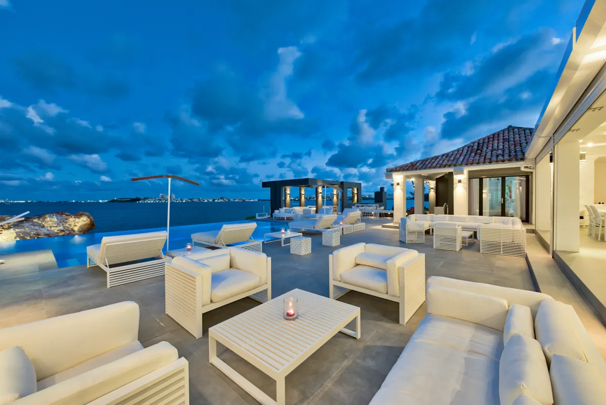 Villa Mirabelle: Outdoor terrace with white lounge furniture beside an infinity pool overlooking the ocean at dusk