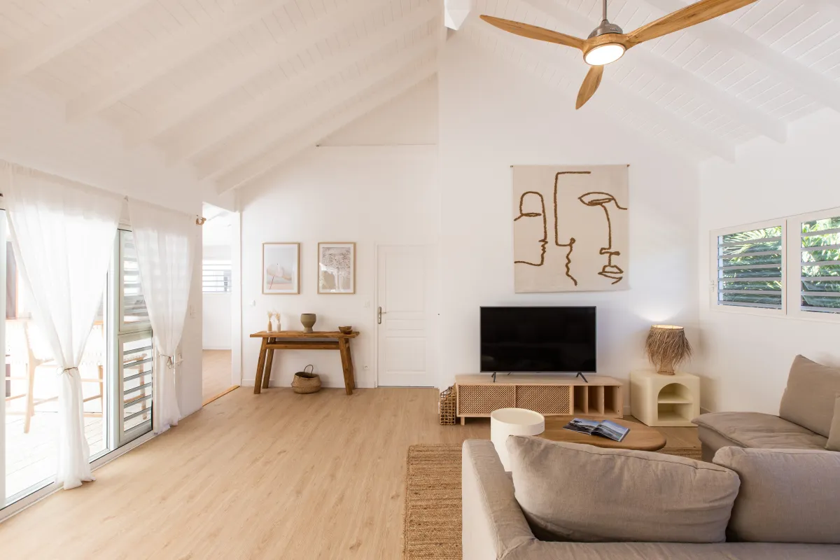 Villa Monchal: Bright living room with vaulted ceiling, neutral sofa, TV console, and light wood floors