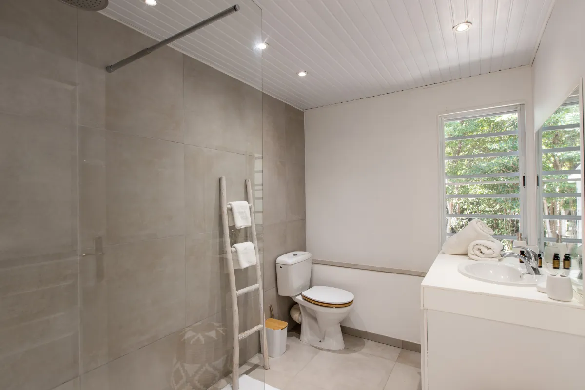 Villa Monchal: Modern bathroom with walk-in shower, toilet, vanity sink, and window overlooking trees
