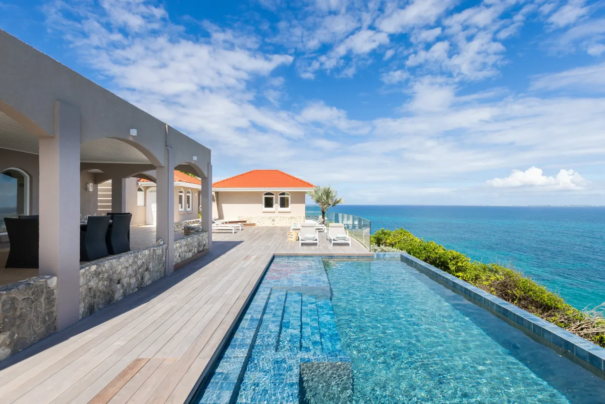Villa Mongoose Run: Infinity pool and wooden sun deck overlooking the ocean under a blue sky
