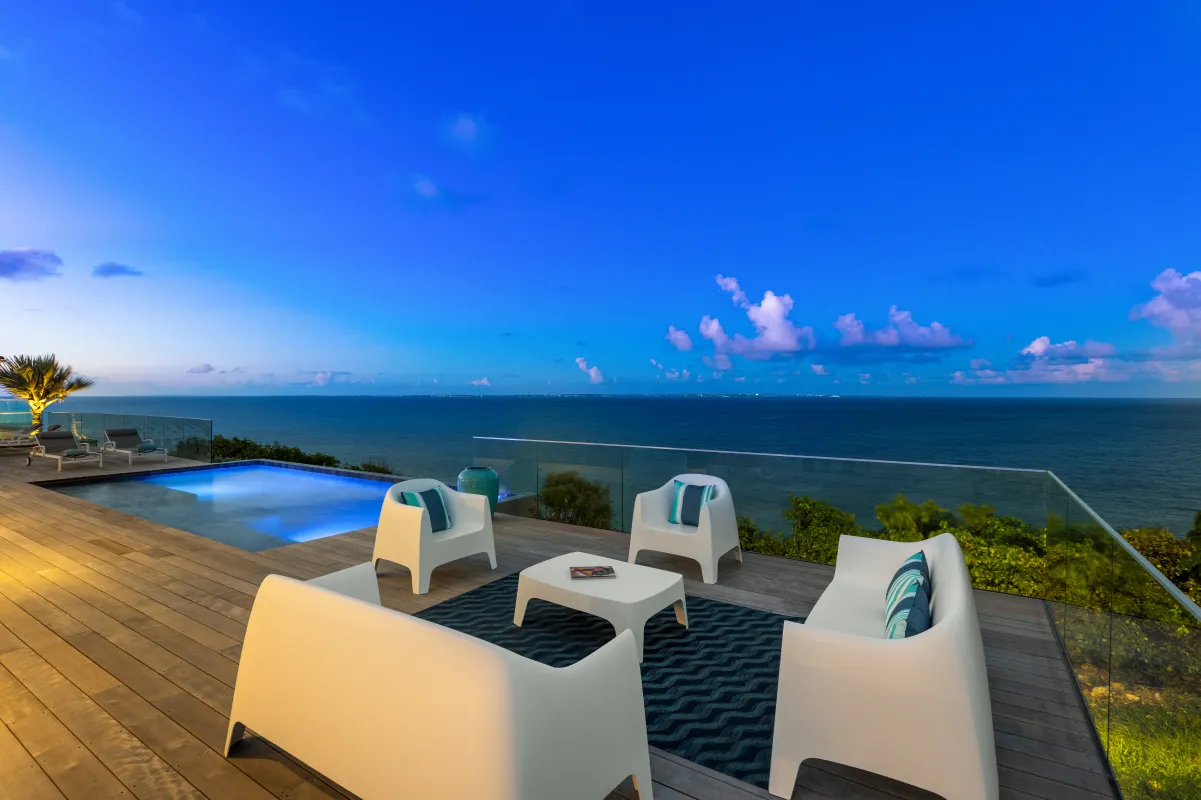 Villa Mongoose Run: Modern outdoor lounge furniture on a wooden deck beside an illuminated pool overlooking the sea