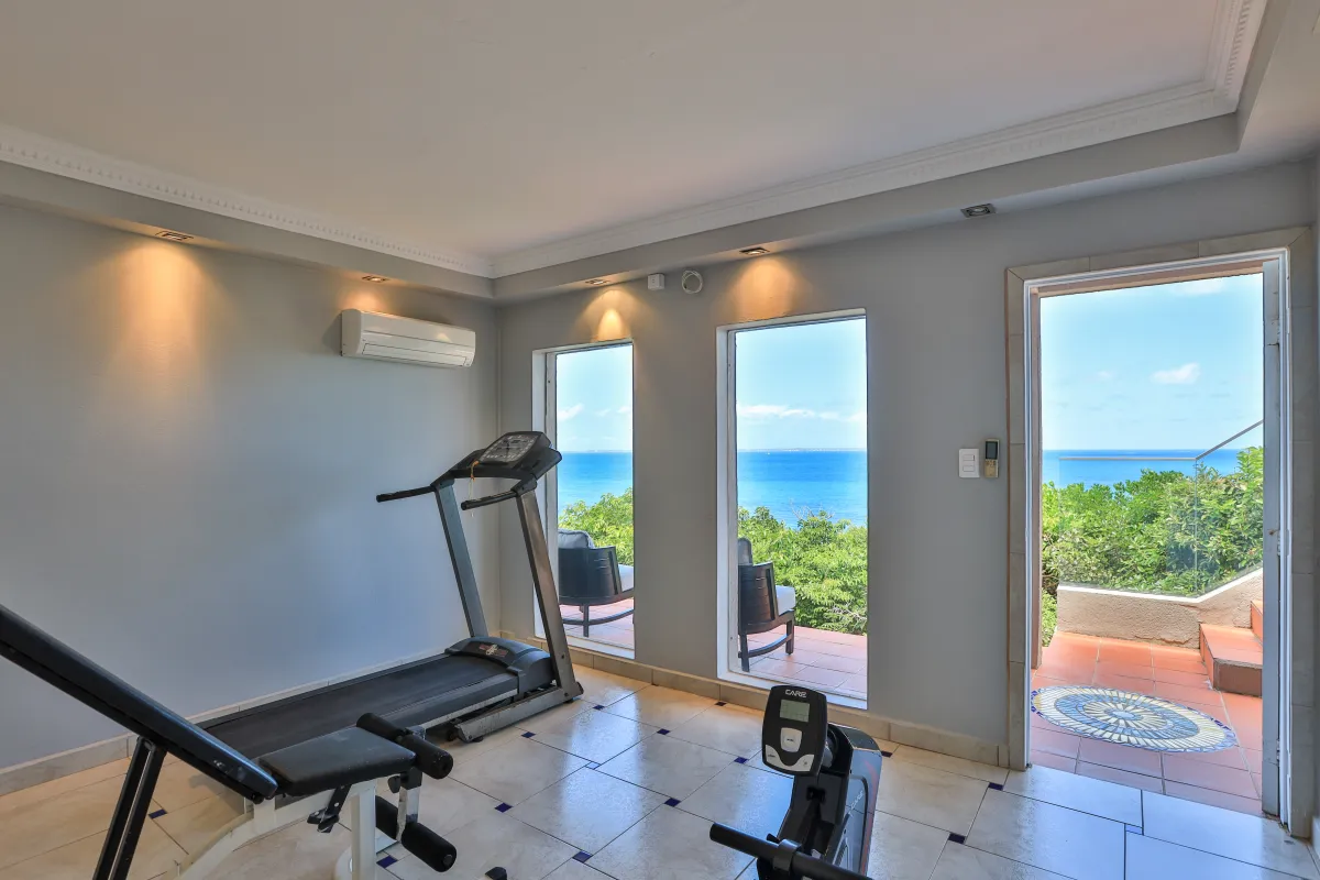 Villa Mongoose Run: Fitness room with workout equipment and windows opening onto a sea view terrace
