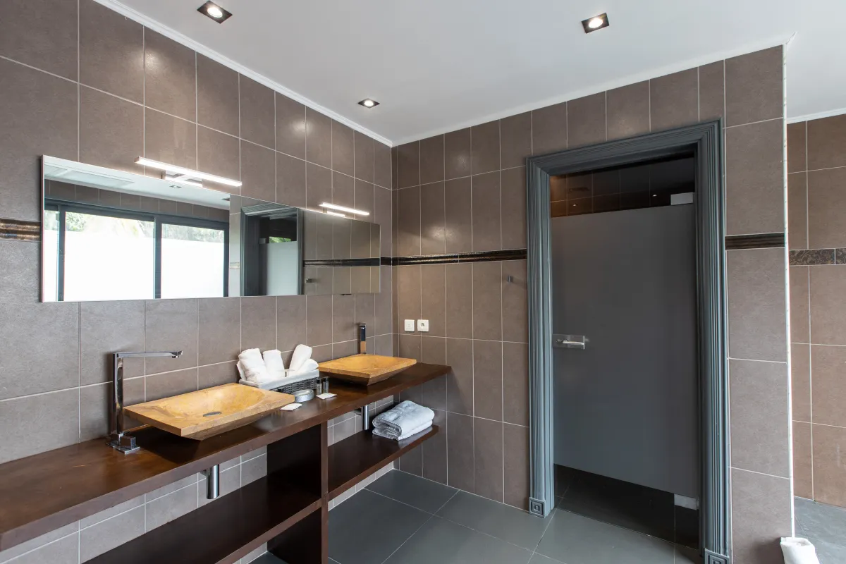 Villa Monte Verde: Bathroom vanity with two stone vessel sinks, wide mirror, and brown tiled walls