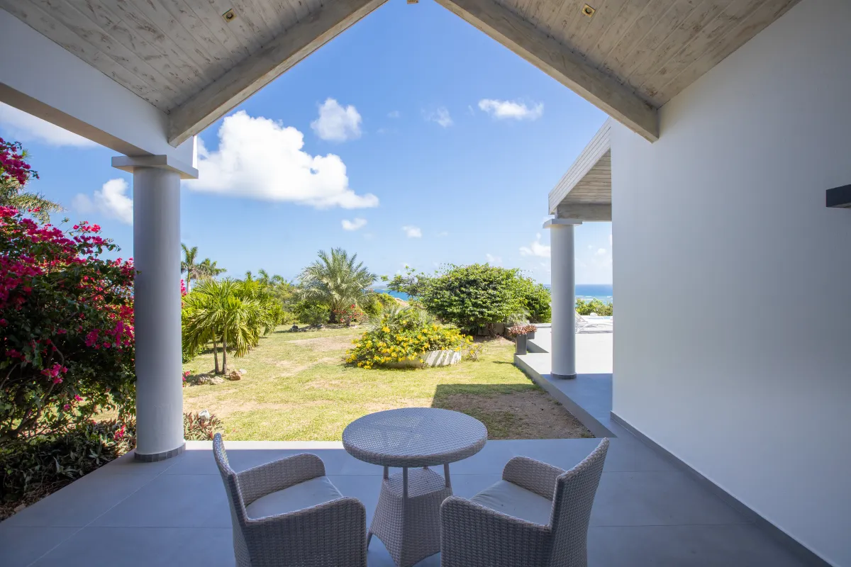 Villa Monte Verde: Covered patio with wicker table and chairs overlooking a tropical garden and distant sea