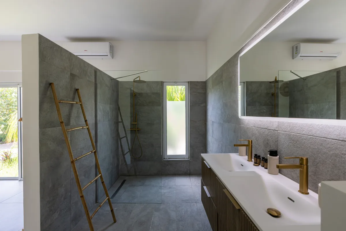 Villa Nirvana: Modern bathroom with walk-in shower, gray tiled walls, and vanity with gold fixtures