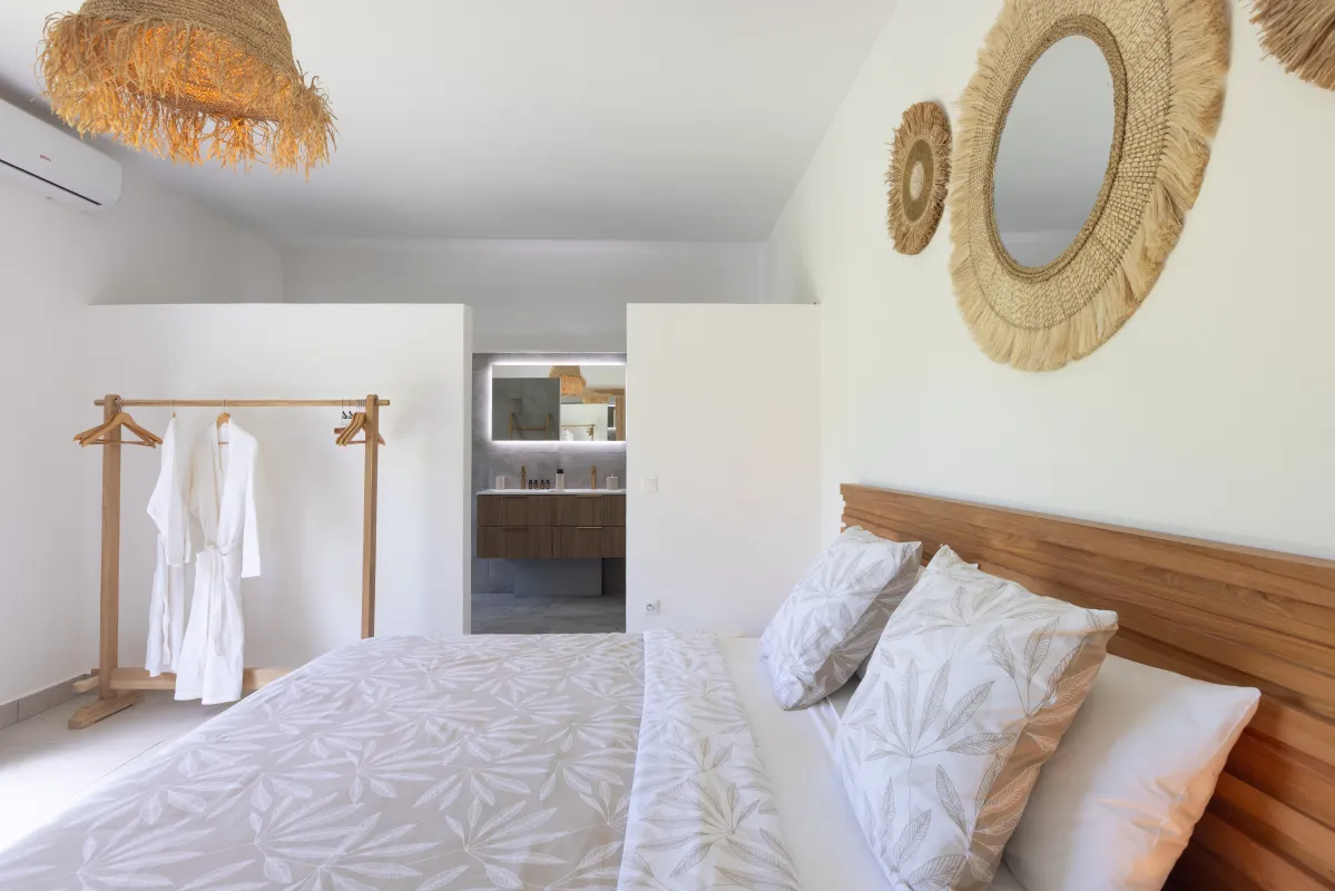 Villa Nirvana: Bright bedroom with wooden headboard, hanging bathrobes, and view into the ensuite bathroom