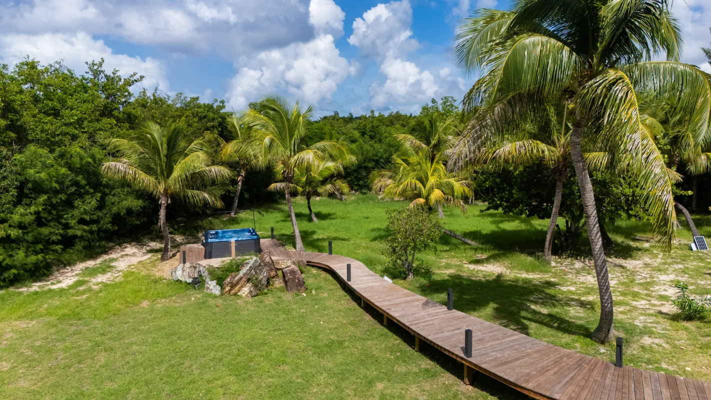 Villa Nirvana: Wooden walkway through a grassy lawn with palm trees leading to an outdoor hot tub