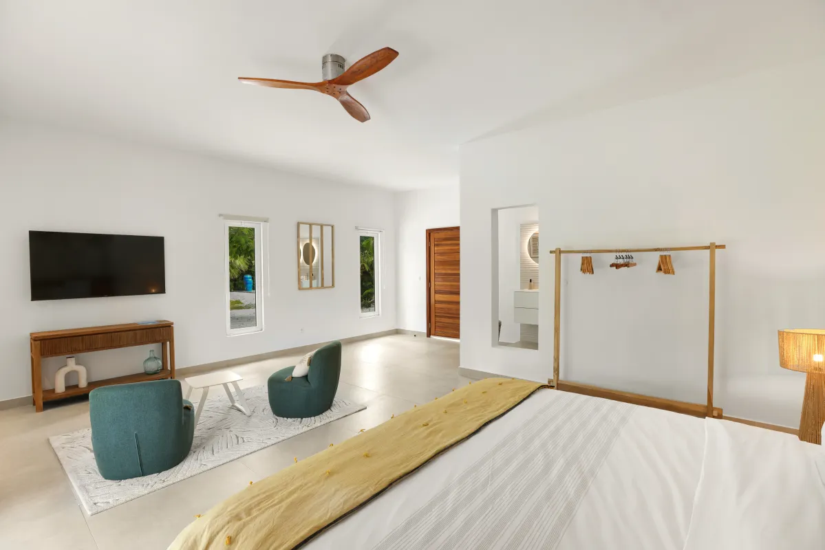 Villa Nirvana: Bedroom with large bed, yellow throw, seating area with two chairs, and wall-mounted television