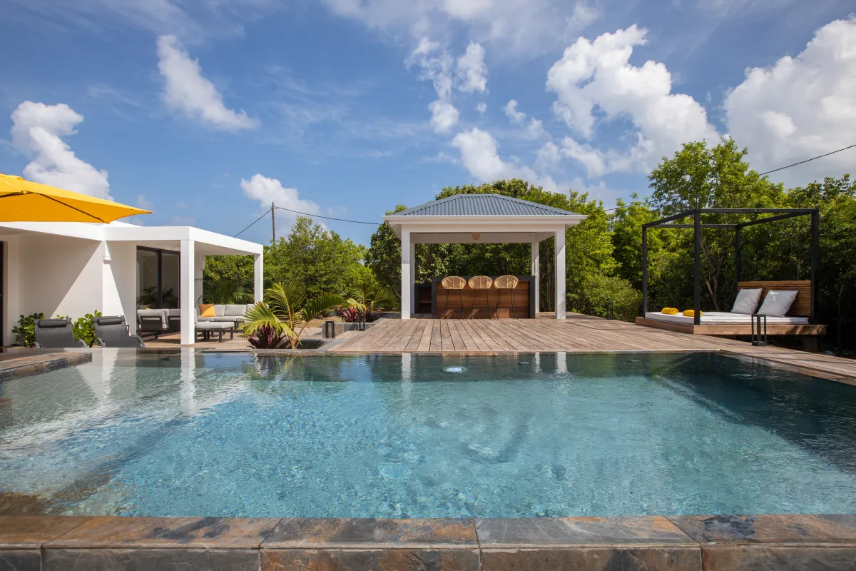 Villa Nuit D'Etoiles: Swimming pool with a wooden deck, outdoor bar gazebo, and daybed under a blue sky