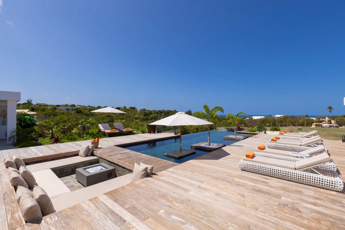 Villa Nuit Jade: Wooden deck with sunken lounge fire pit, swimming pool, and sun loungers under blue sky