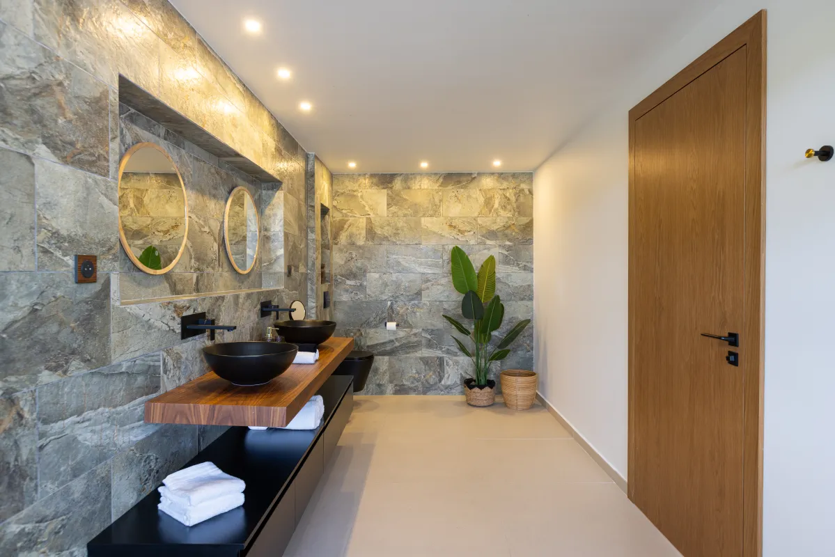 Villa Nuit Jade: Modern bathroom with double vessel sinks, round mirrors, and stone tiled walls