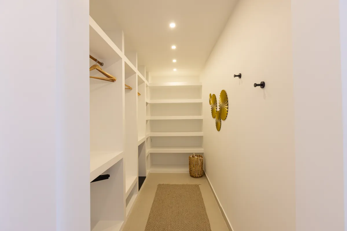 Villa Nuit Jade: Walk-in closet with built-in white shelving, hanging racks, and a woven runner rug