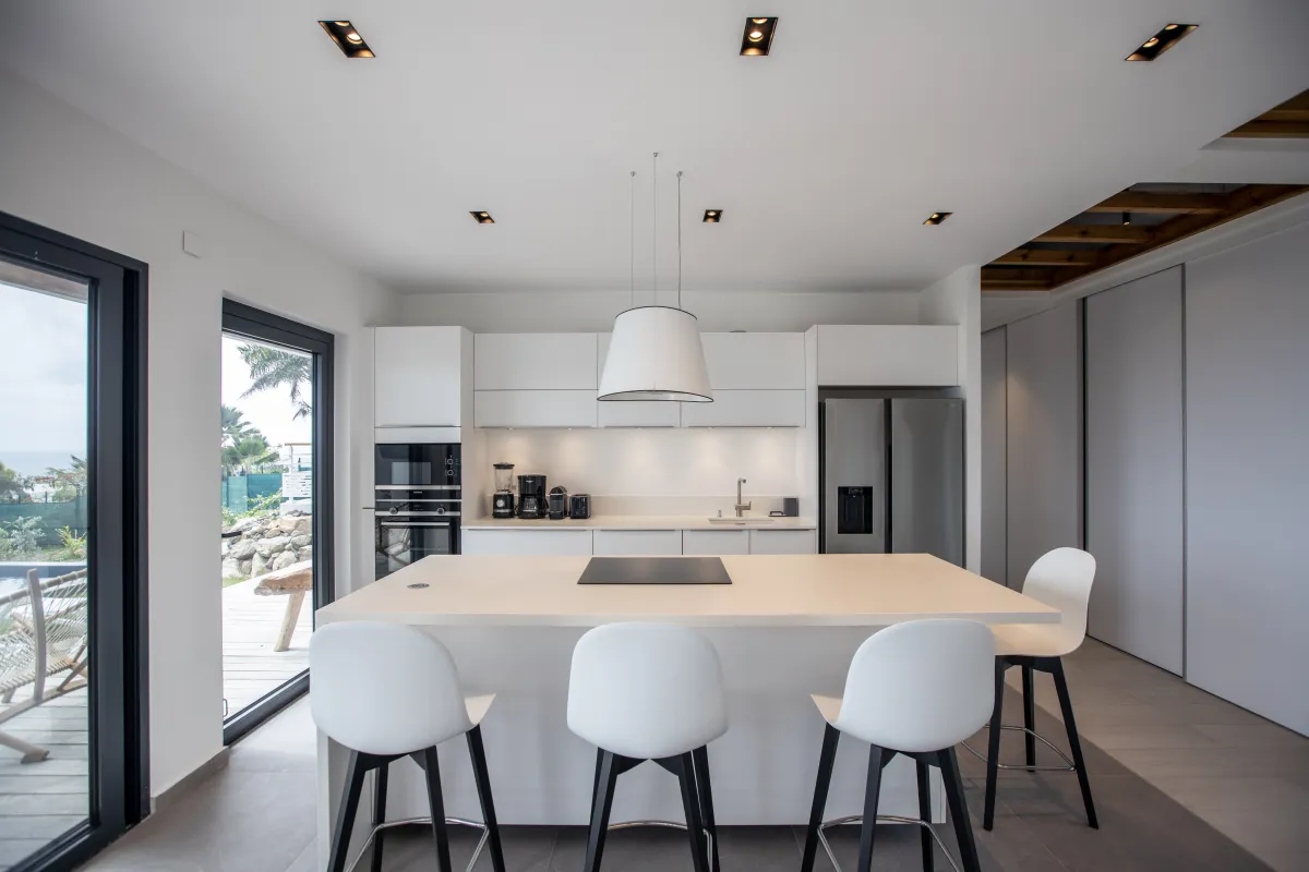Villa Ocean's One: Modern white kitchen with an island, bar stools, and sliding doors to the terrace