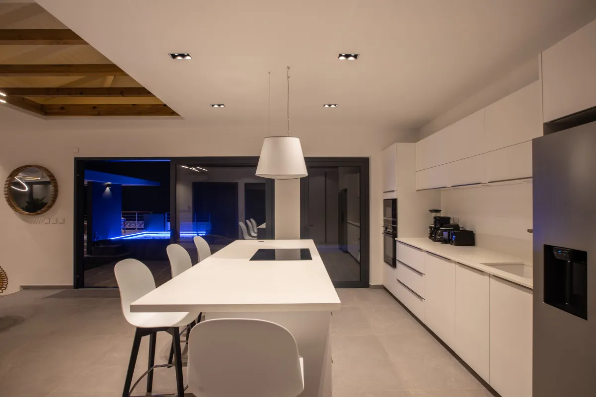 Villa Ocean's One: Modern kitchen with white island, bar stools, and sliding doors to the terrace