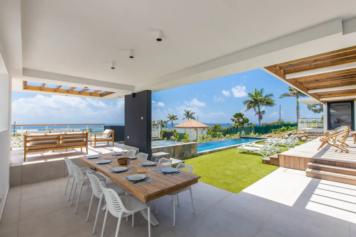 Villa Ocean's One: Covered terrace with outdoor dining table overlooking a swimming pool, lawn, and ocean