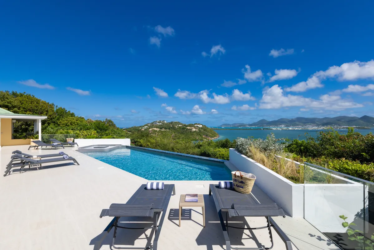 Villa Osun: Sun loungers on a terrace by an infinity pool overlooking a coastal bay and hills